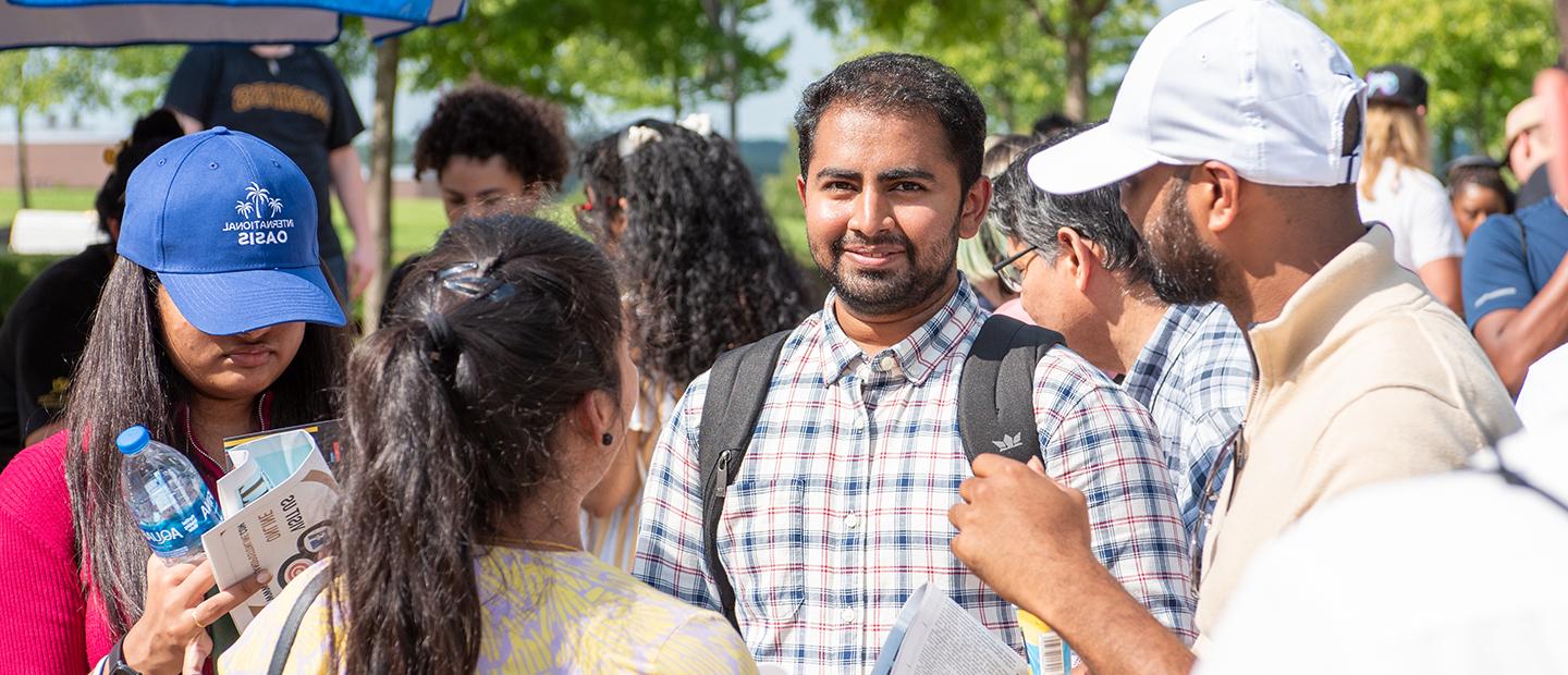 A young man wearing a backpack stands with a group of people smiling