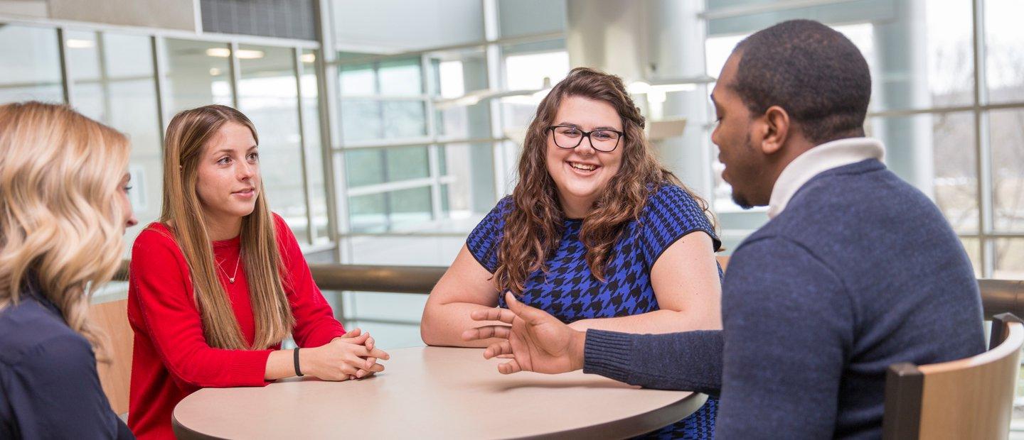 four students seated at a table with windows behind them